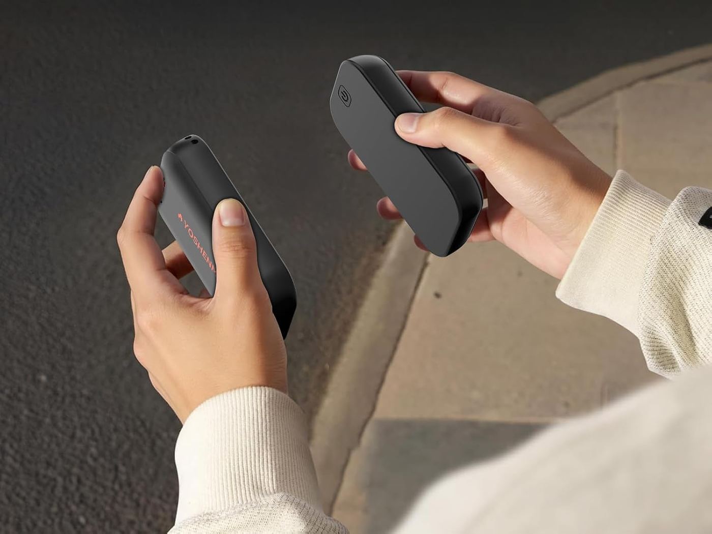 Two hands holding black pocket hand warmers outdoors at night